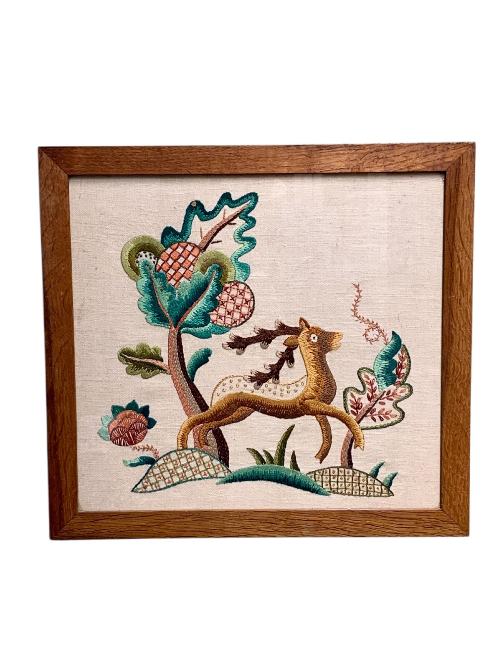 A square wooden frame enclosing a 1930s crewelwork embroidery depicting a leaping stag beside a stylised tree on a cream linen background.