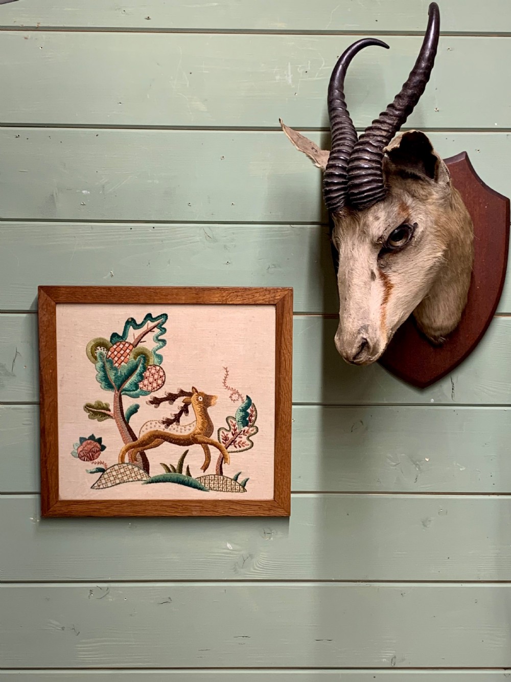 A square wooden frame enclosing a 1930s crewelwork embroidery depicting a leaping stag beside a stylised tree on a cream linen background. View II