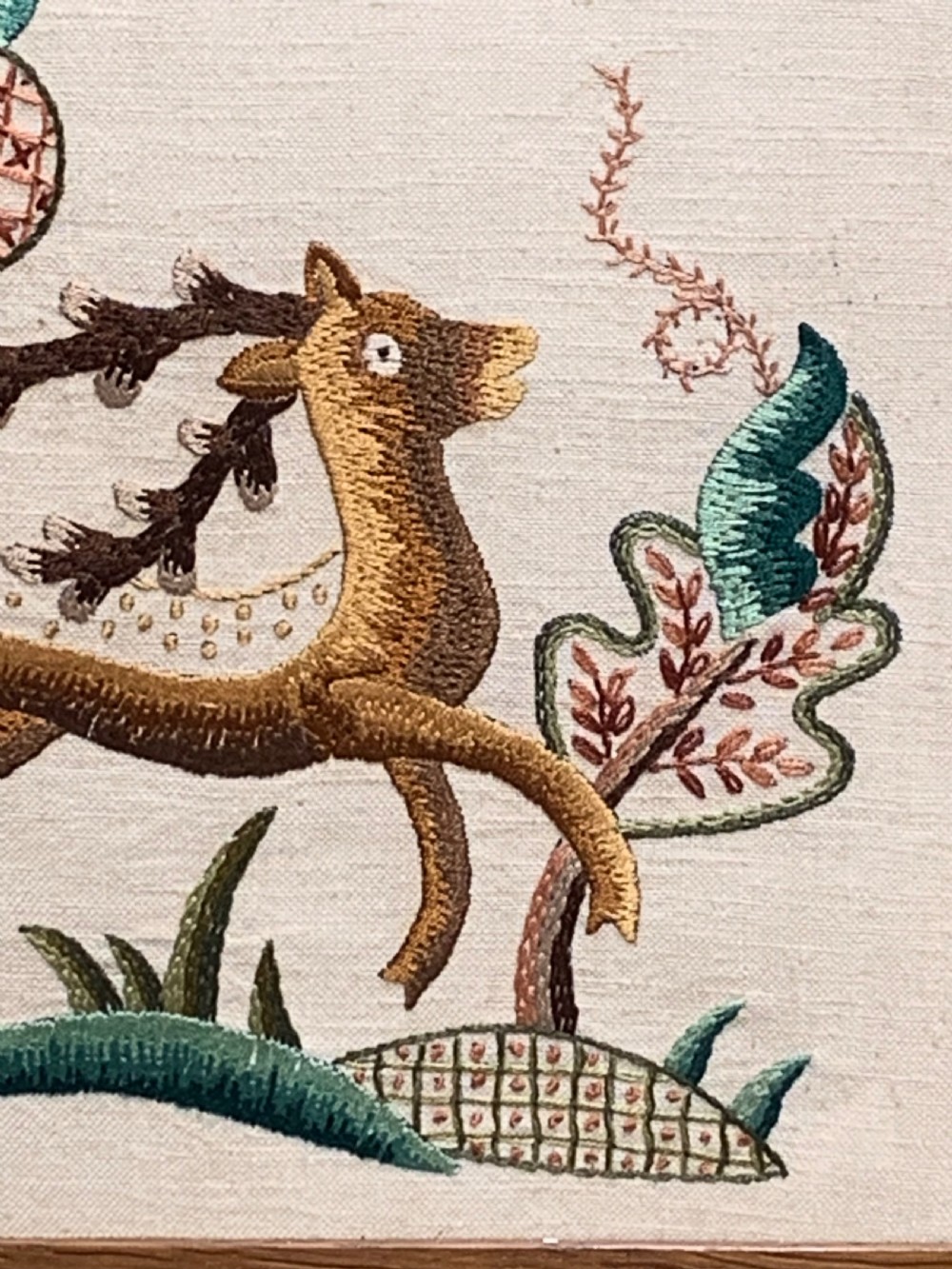 A square wooden frame enclosing a 1930s crewelwork embroidery depicting a leaping stag beside a stylised tree on a cream linen background. View III