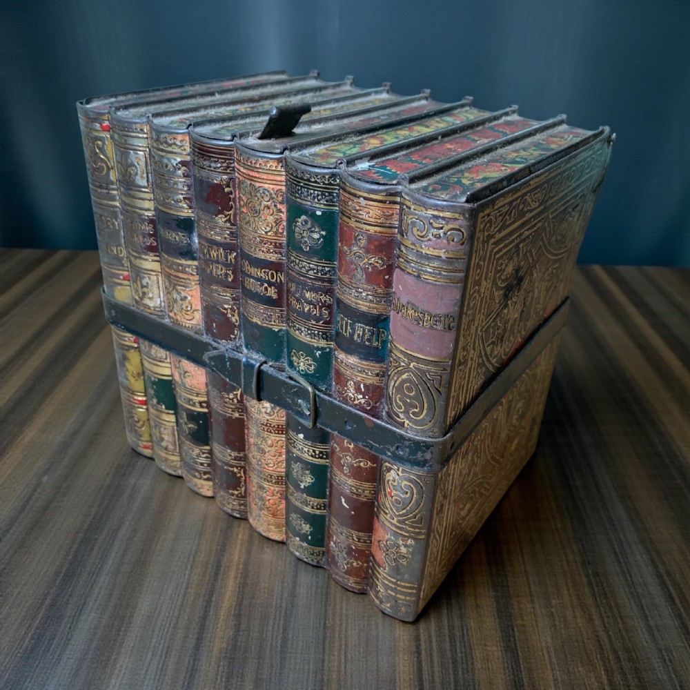 An Edwardian lithographed tinplate biscuit box designed to resemble a row of classic leather-bound books held together by a faux strap.