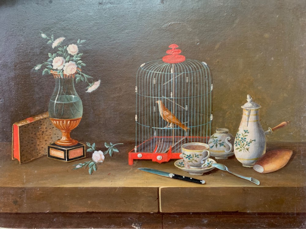An early nineteenth-century framed French gouache still-life painting depicting a tabletop scene with a bird in a cage, a floral vase, porcelain teaware, and a book set within a carved giltwood frame. View II