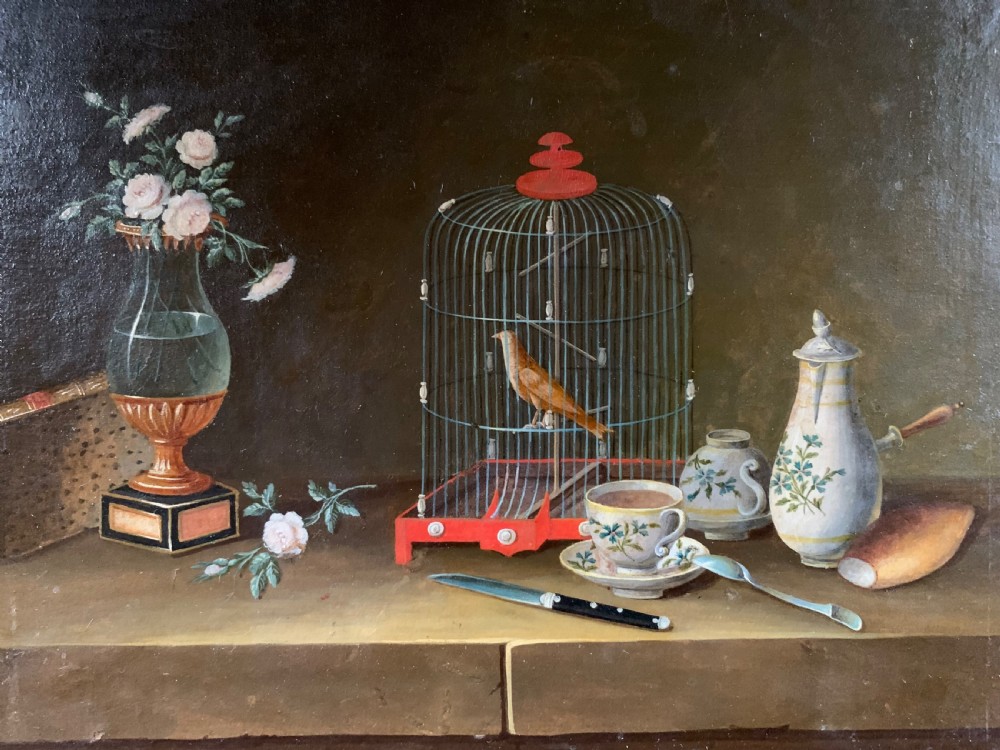 An early nineteenth-century framed French gouache still-life painting depicting a tabletop scene with a bird in a cage, a floral vase, porcelain teaware, and a book set within a carved giltwood frame. View III
