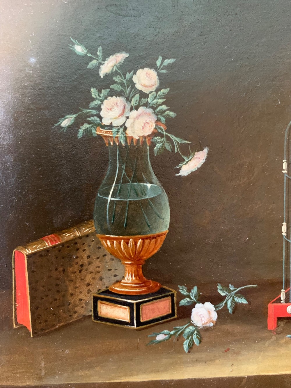 An early nineteenth-century framed French gouache still-life painting depicting a tabletop scene with a bird in a cage, a floral vase, porcelain teaware, and a book set within a carved giltwood frame. View V