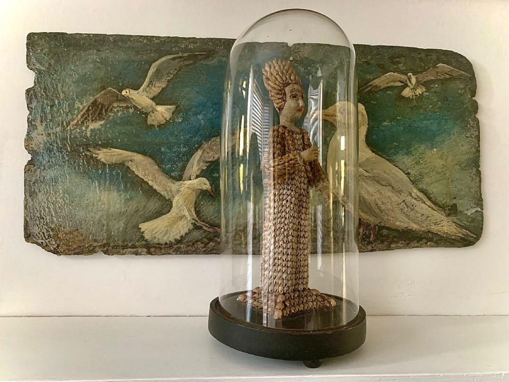 A standing figure of a woman sculpted from tiny arranged seashells on a circular dark wood base. View II