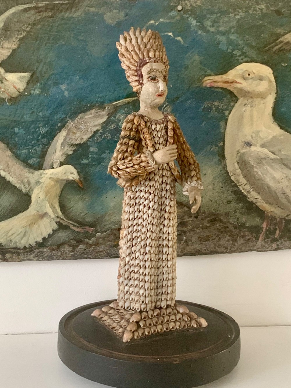 A standing figure of a woman sculpted from tiny arranged seashells on a circular dark wood base. View IV
