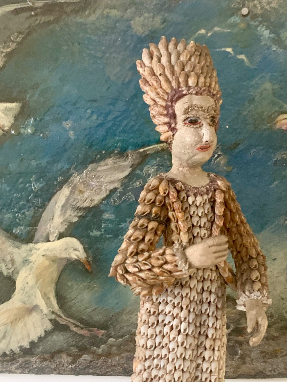 A standing figure of a woman sculpted from tiny arranged seashells on a circular dark wood base. View V
