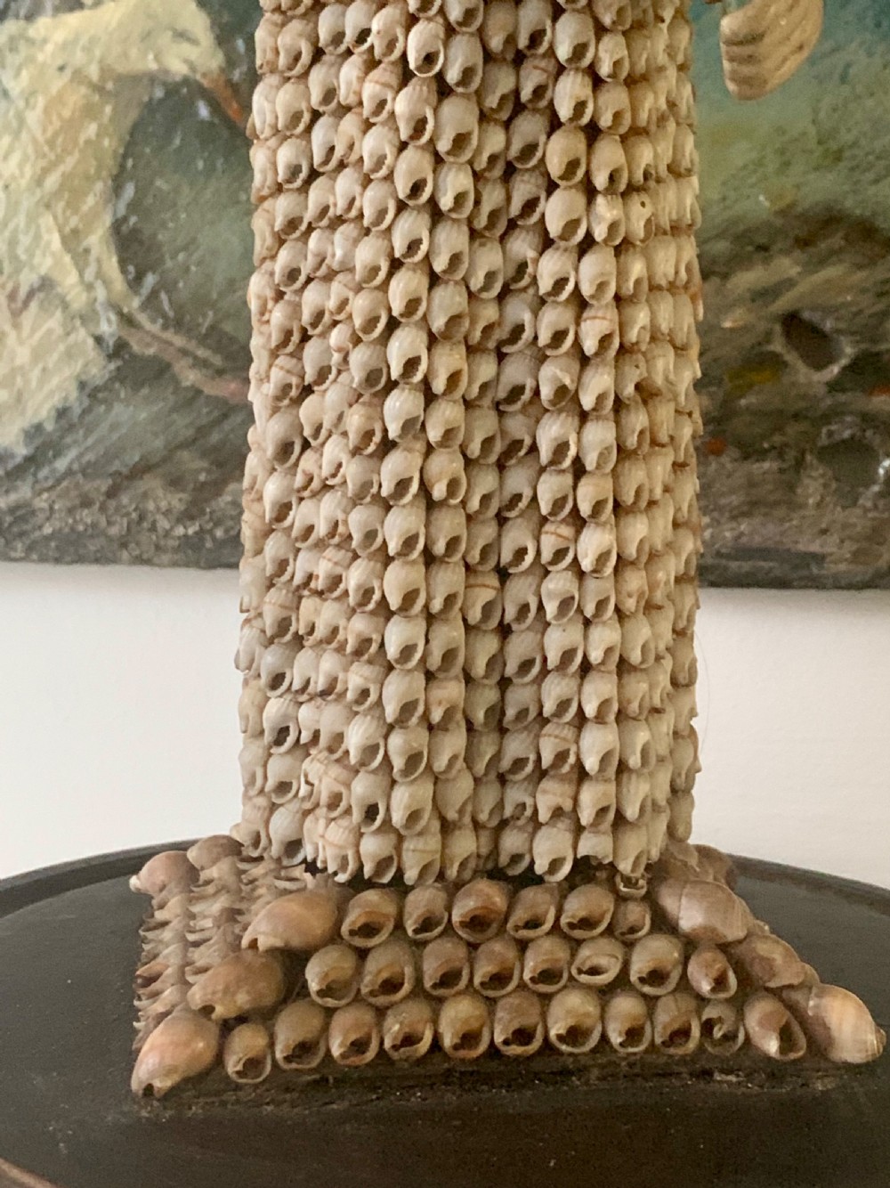 A standing figure of a woman sculpted from tiny arranged seashells on a circular dark wood base. View VI