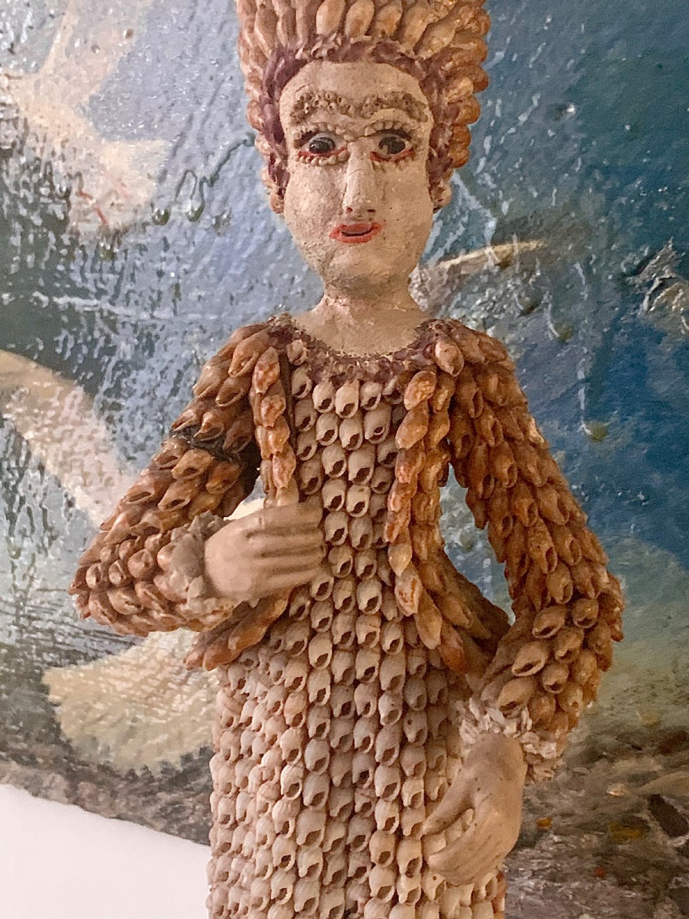 A standing figure of a woman sculpted from tiny arranged seashells on a circular dark wood base. View VII