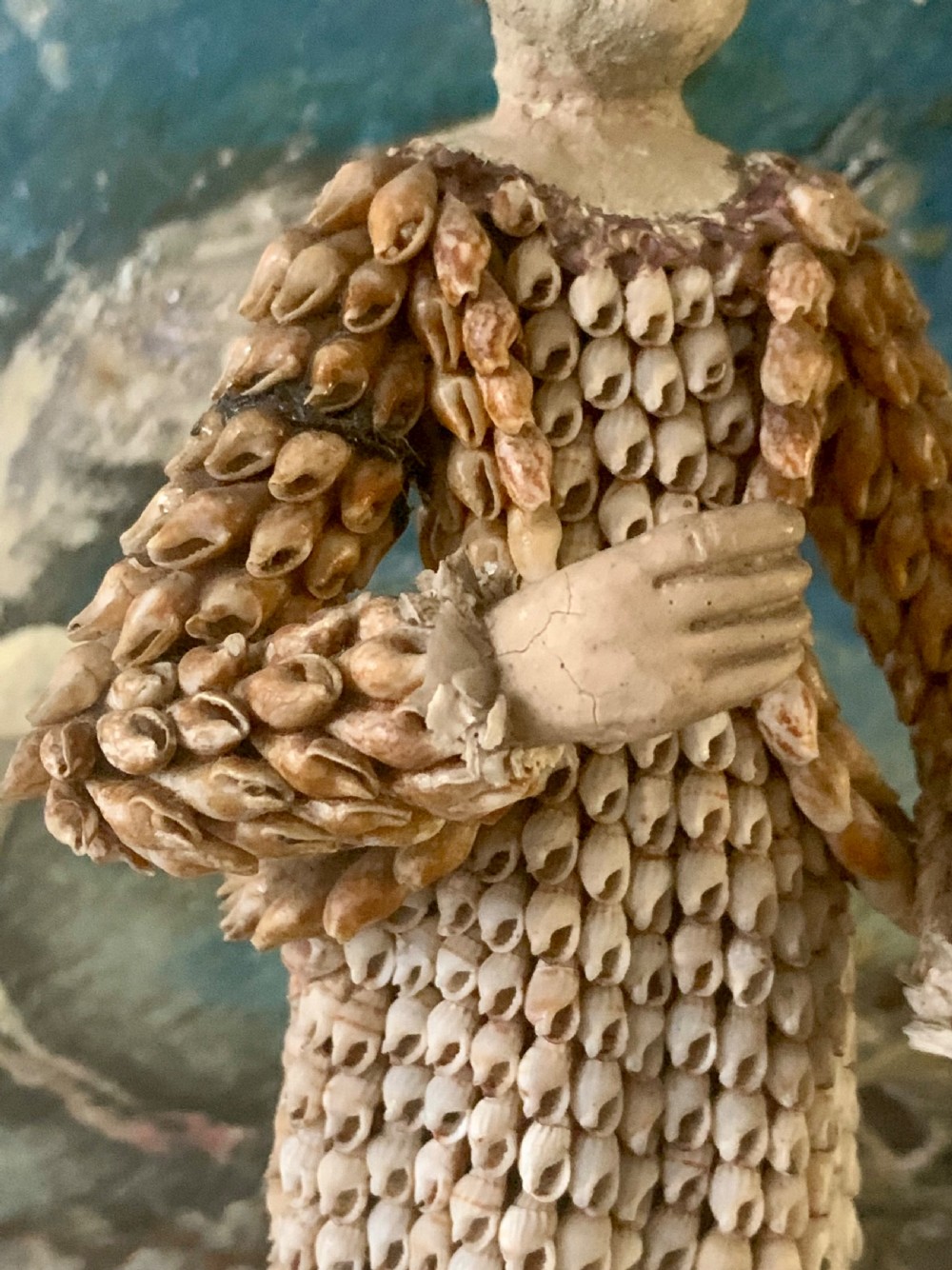 A standing figure of a woman sculpted from tiny arranged seashells on a circular dark wood base. View IX