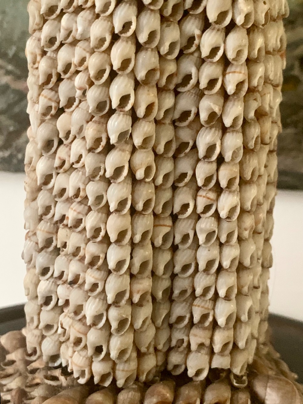 A standing figure of a woman sculpted from tiny arranged seashells on a circular dark wood base. View X