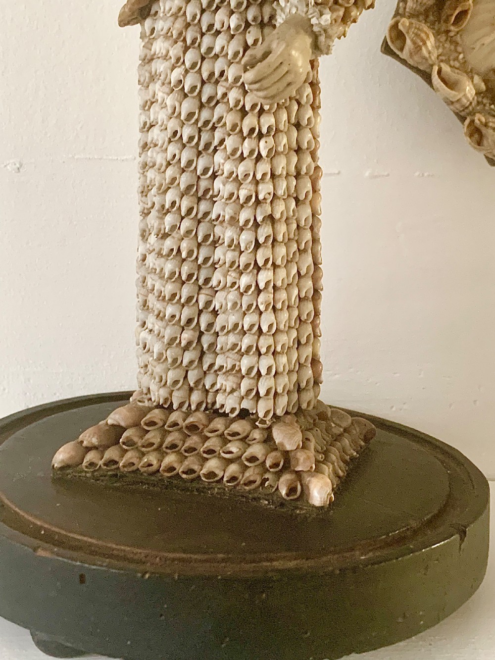 A standing figure of a woman sculpted from tiny arranged seashells on a circular dark wood base. View XI