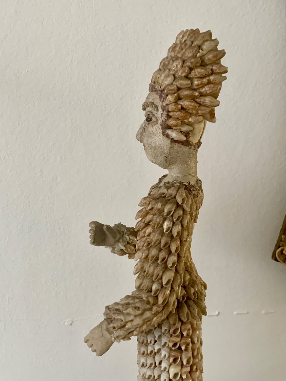 A standing figure of a woman sculpted from tiny arranged seashells on a circular dark wood base. View XII