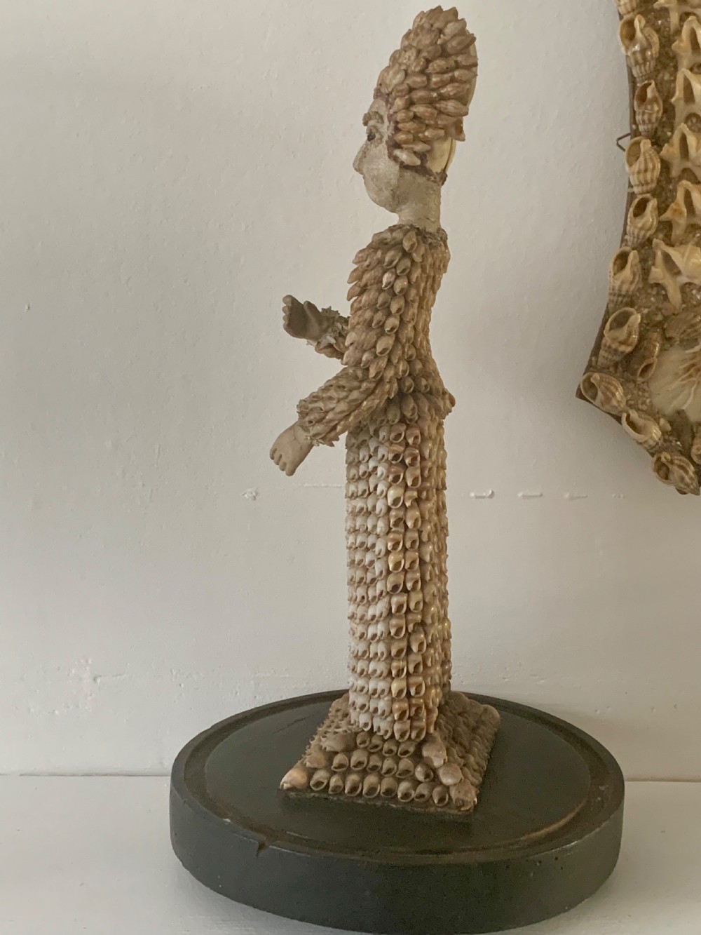 A standing figure of a woman sculpted from tiny arranged seashells on a circular dark wood base. View XIII