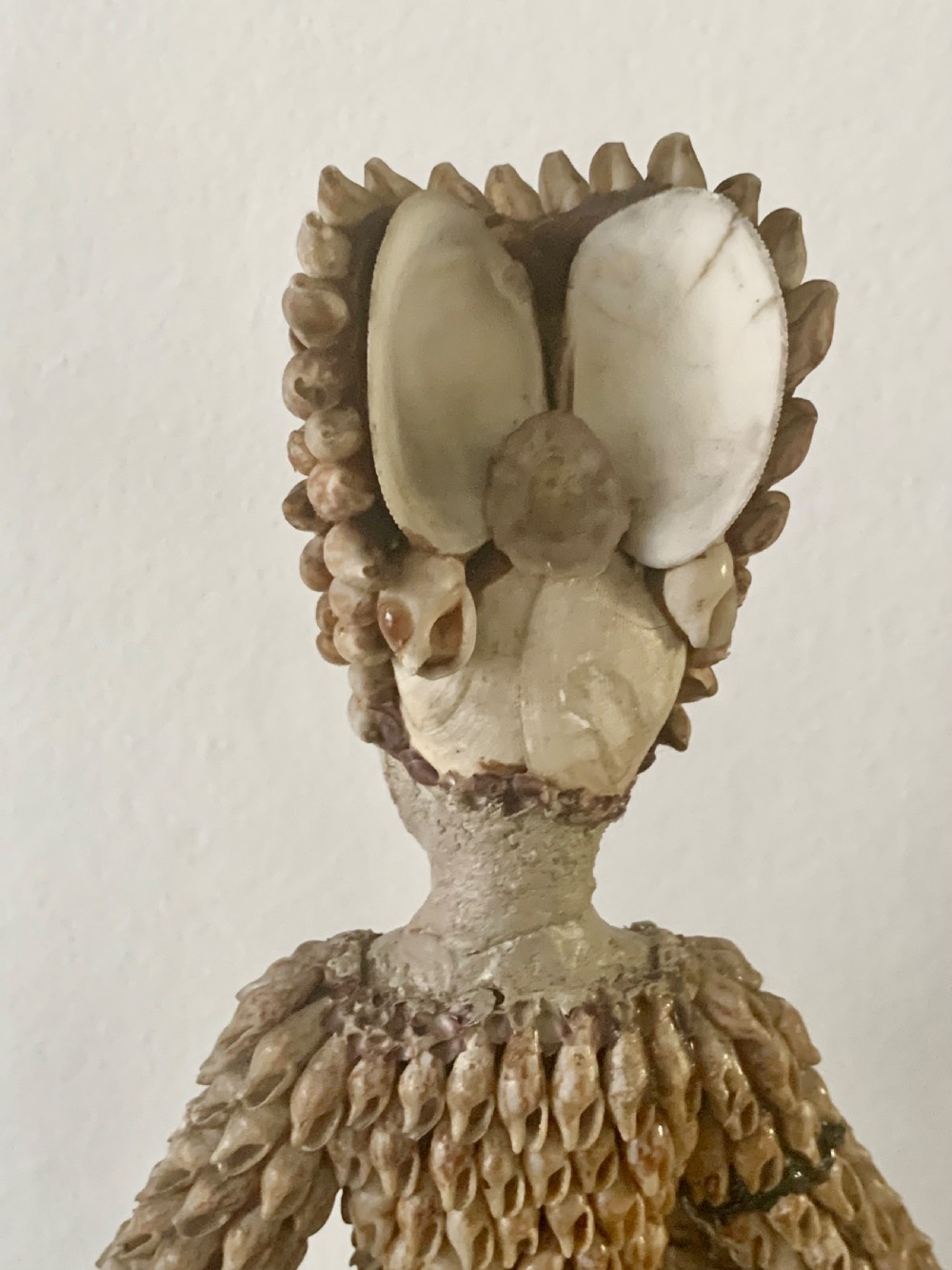 A standing figure of a woman sculpted from tiny arranged seashells on a circular dark wood base. View XIV
