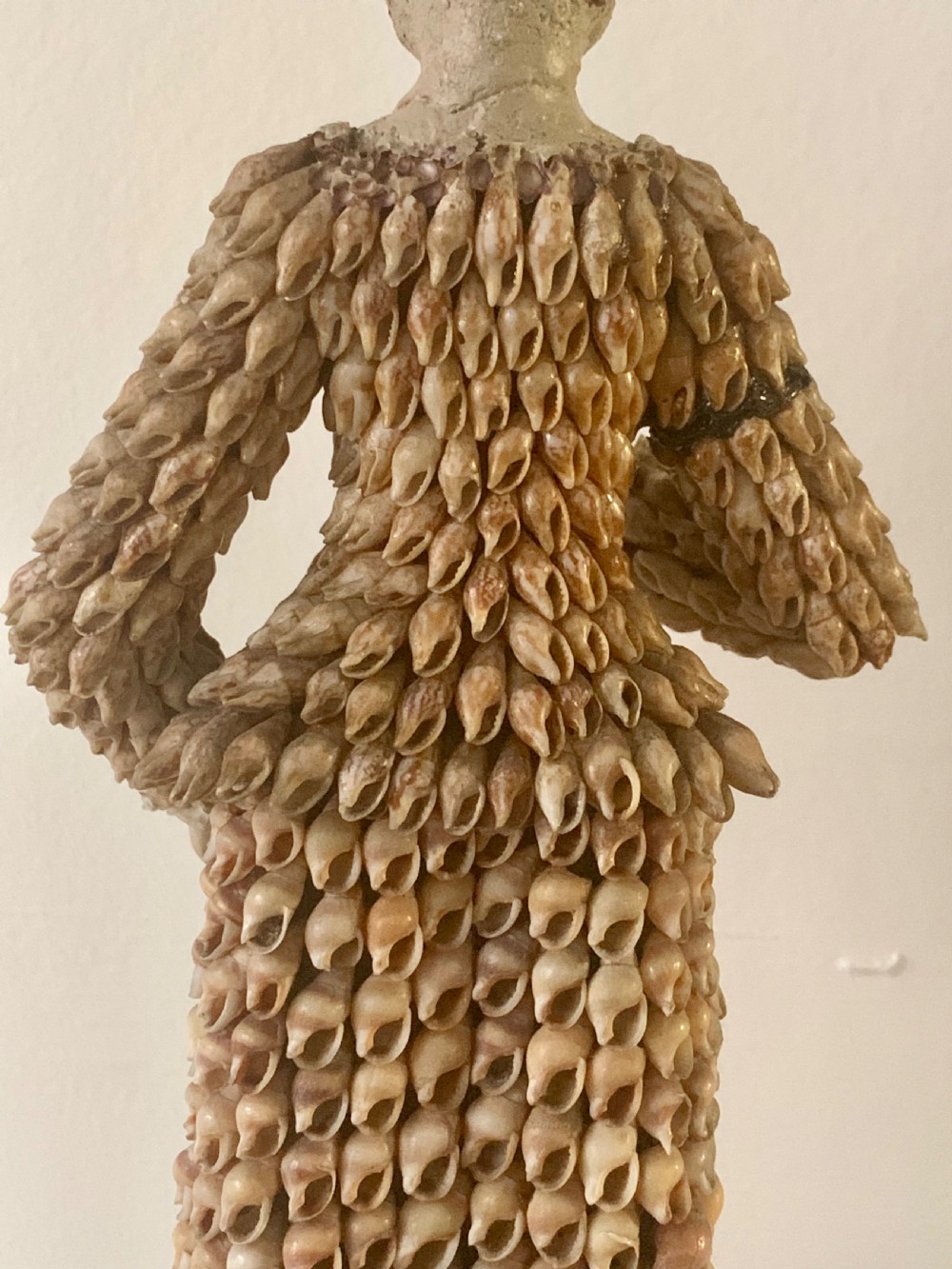 A standing figure of a woman sculpted from tiny arranged seashells on a circular dark wood base. View XV