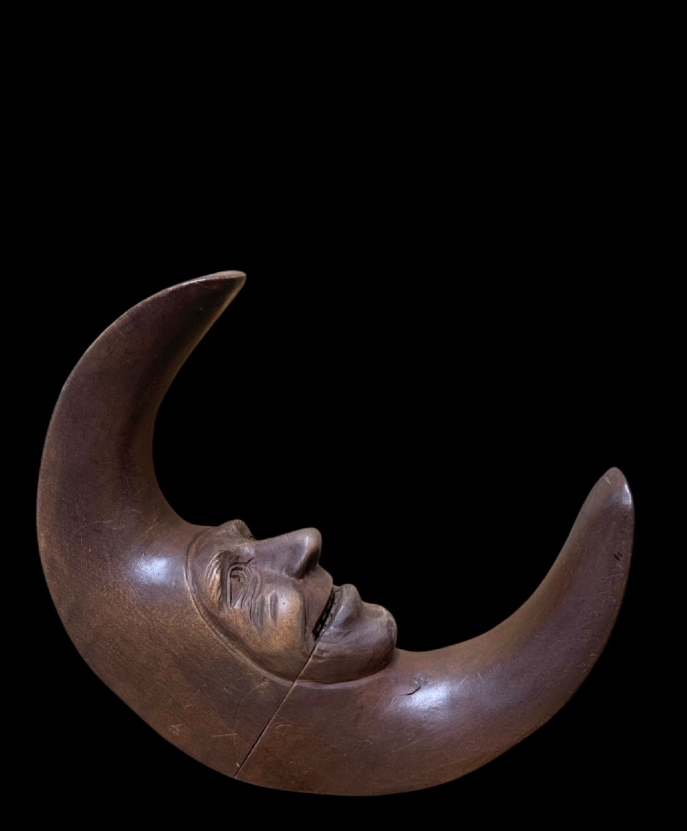 A dark brown carved wooden nutcracker shaped like a crescent moon with a human facial profile carved into the inner curve.