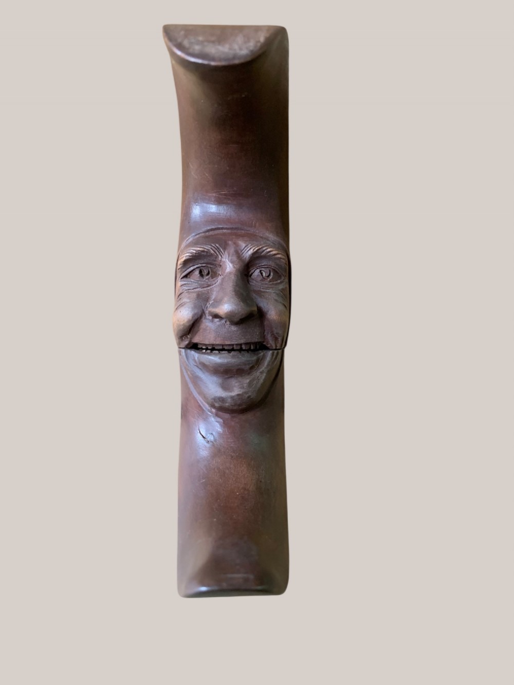A dark brown carved wooden nutcracker shaped like a crescent moon with a human facial profile carved into the inner curve. View III