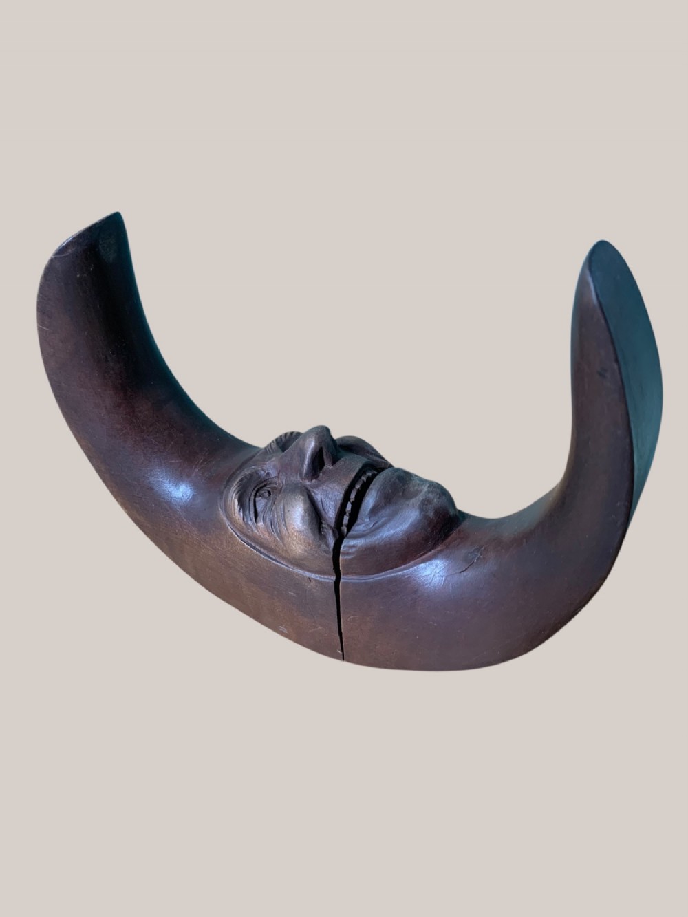 A dark brown carved wooden nutcracker shaped like a crescent moon with a human facial profile carved into the inner curve. View IV