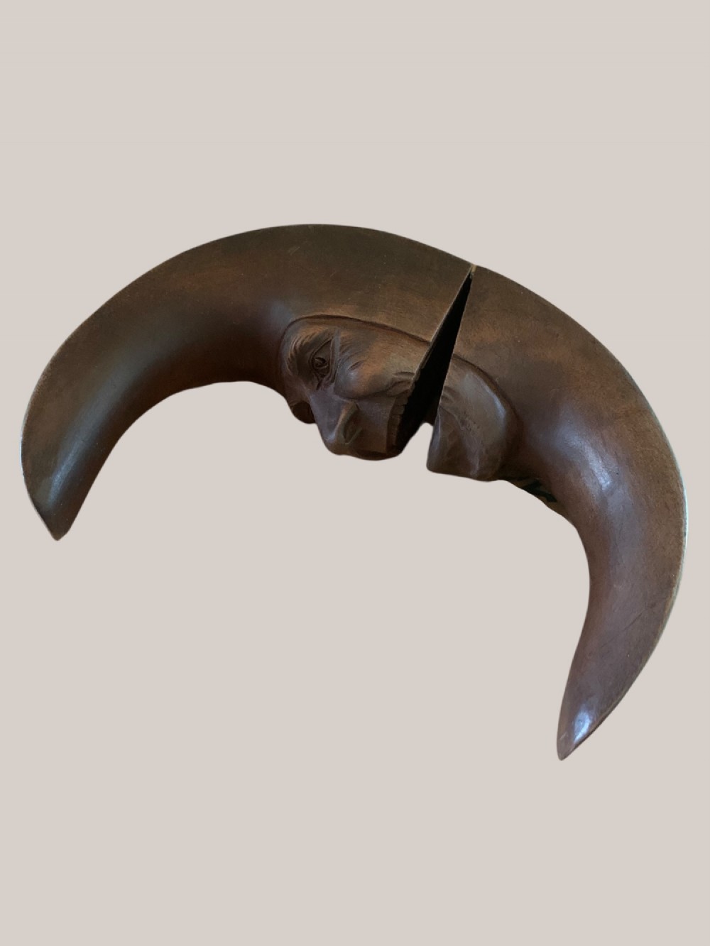 A dark brown carved wooden nutcracker shaped like a crescent moon with a human facial profile carved into the inner curve. View V