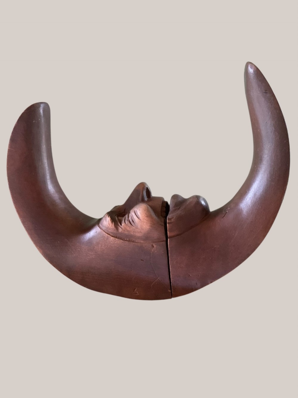 A dark brown carved wooden nutcracker shaped like a crescent moon with a human facial profile carved into the inner curve. View VII