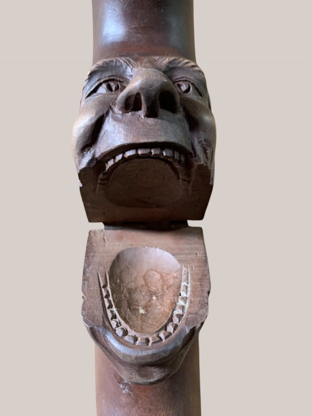 A dark brown carved wooden nutcracker shaped like a crescent moon with a human facial profile carved into the inner curve. View X