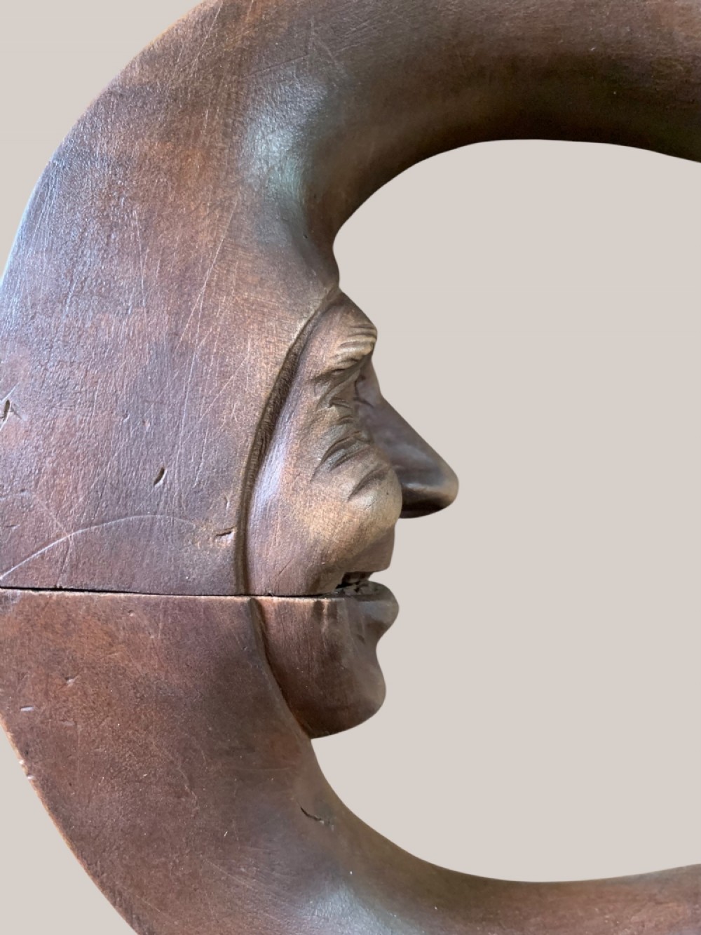 A dark brown carved wooden nutcracker shaped like a crescent moon with a human facial profile carved into the inner curve. View XII