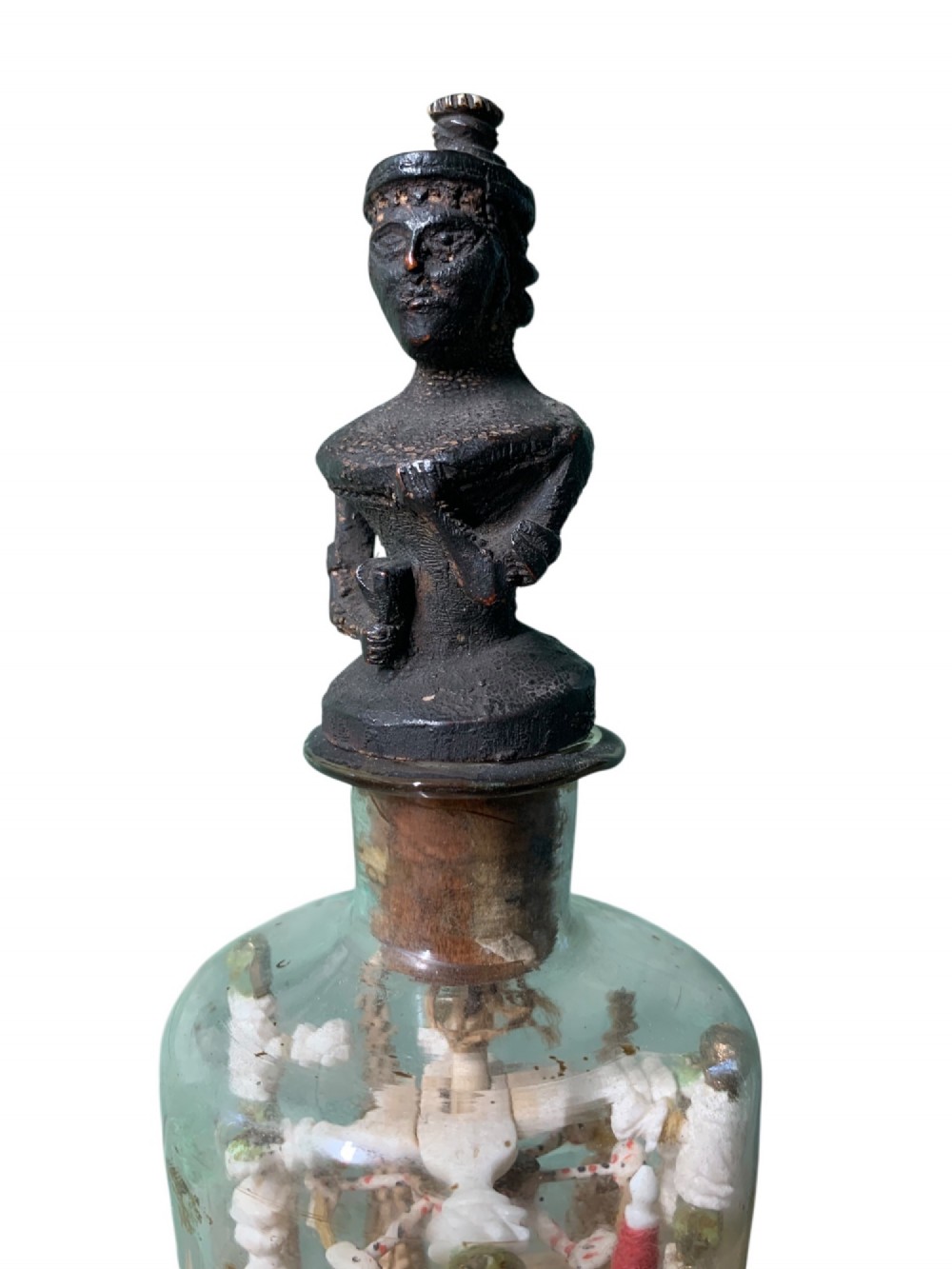 A clear glass bottle housing a detailed hand-carved bone miniature structure inside, topped with a cork and a dark carved bust finial stopper. View IV