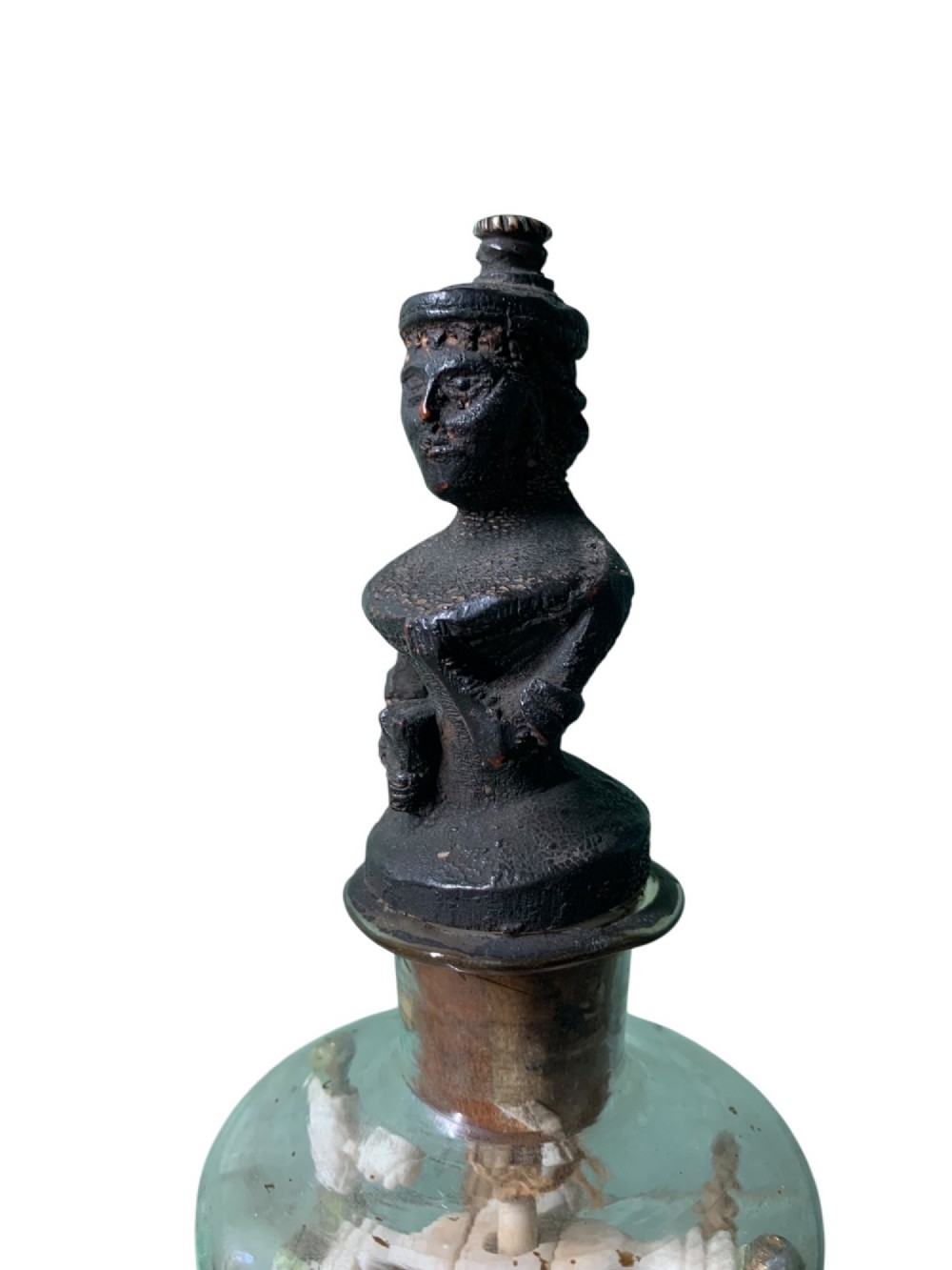 A clear glass bottle housing a detailed hand-carved bone miniature structure inside, topped with a cork and a dark carved bust finial stopper. View V