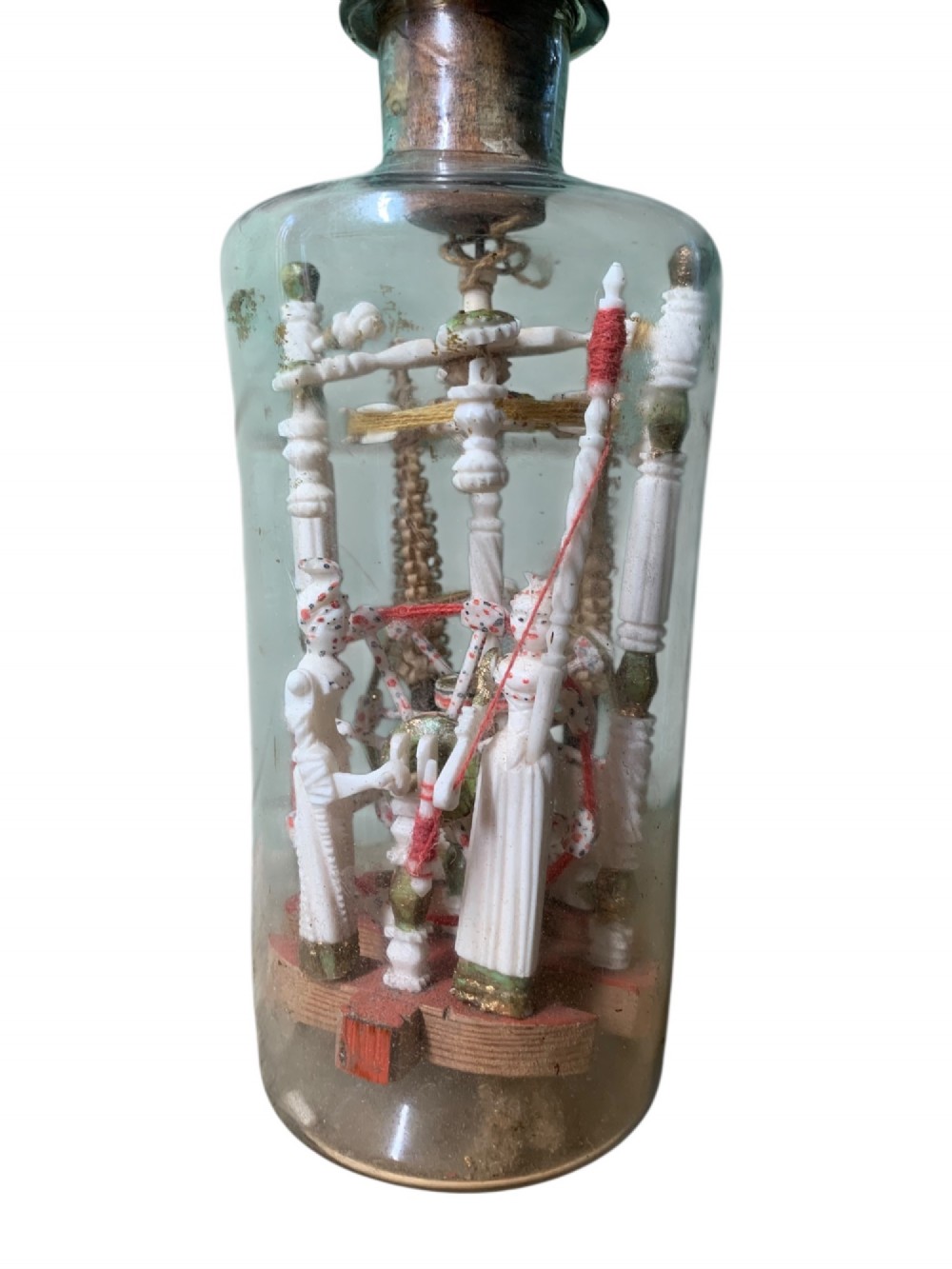 A clear glass bottle housing a detailed hand-carved bone miniature structure inside, topped with a cork and a dark carved bust finial stopper. View VII