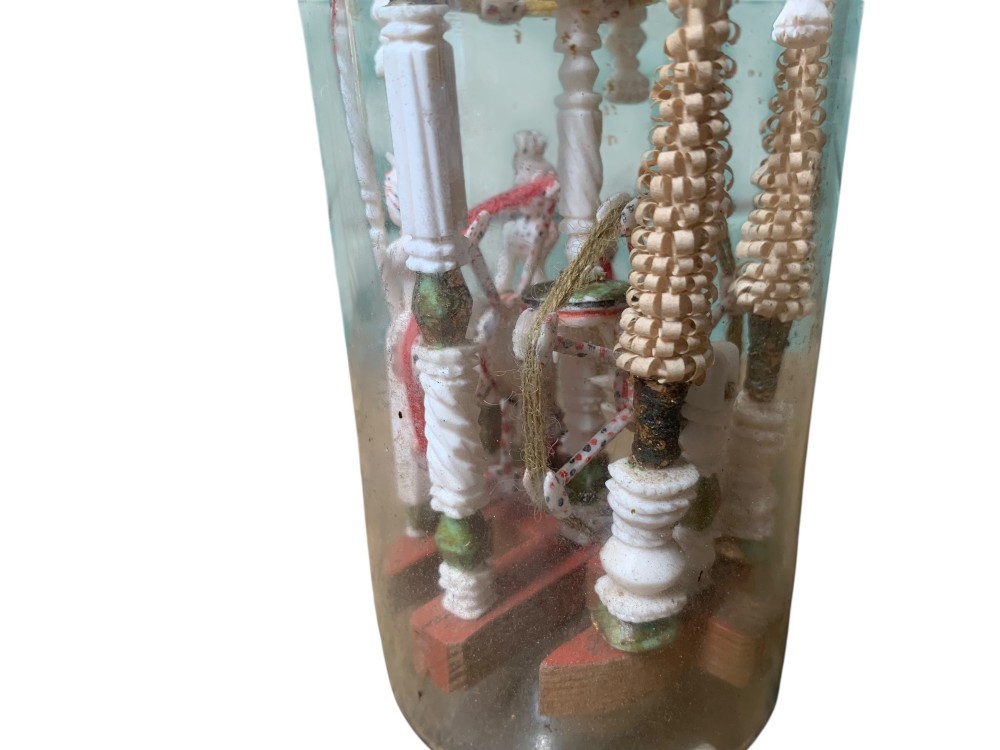 A clear glass bottle housing a detailed hand-carved bone miniature structure inside, topped with a cork and a dark carved bust finial stopper. View IX