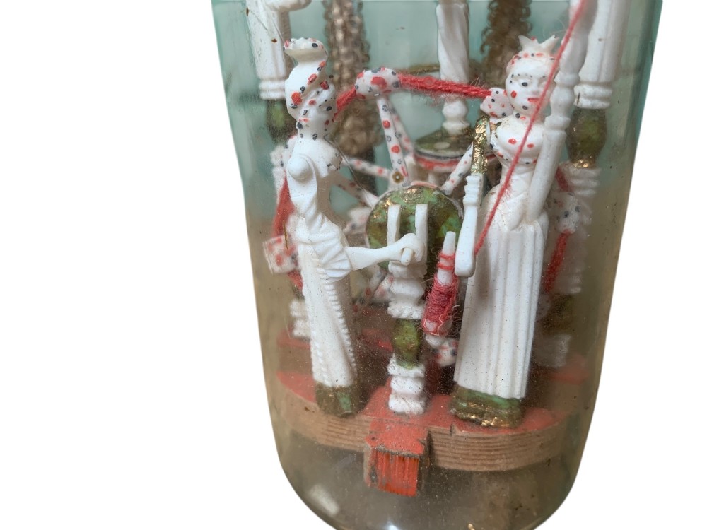 A clear glass bottle housing a detailed hand-carved bone miniature structure inside, topped with a cork and a dark carved bust finial stopper. View X