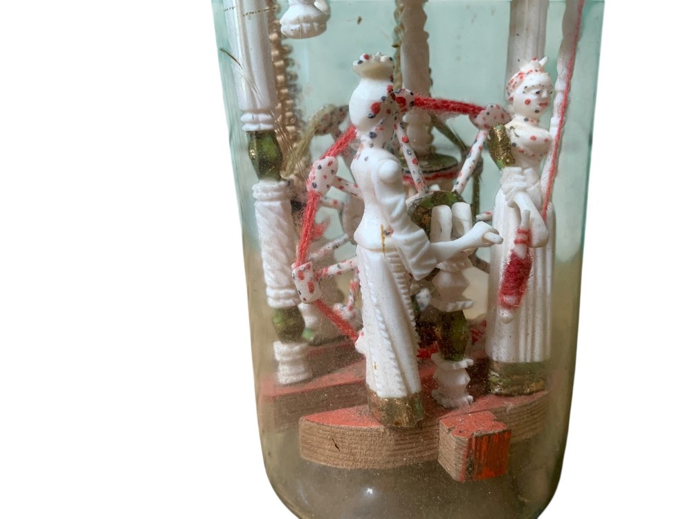 A clear glass bottle housing a detailed hand-carved bone miniature structure inside, topped with a cork and a dark carved bust finial stopper. View XI