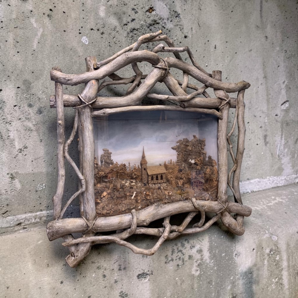 An antique three-dimensional cork diorama depicting a village church scene enclosed within a frame crafted from intertwined rustic twigs.