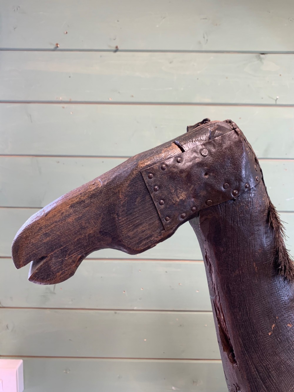 A naive hand-carved dark wood figure of a horse mounted on a flat wooden base with four simple circular wheels. View II