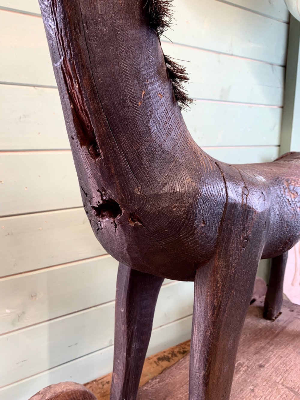 A naive hand-carved dark wood figure of a horse mounted on a flat wooden base with four simple circular wheels. View V