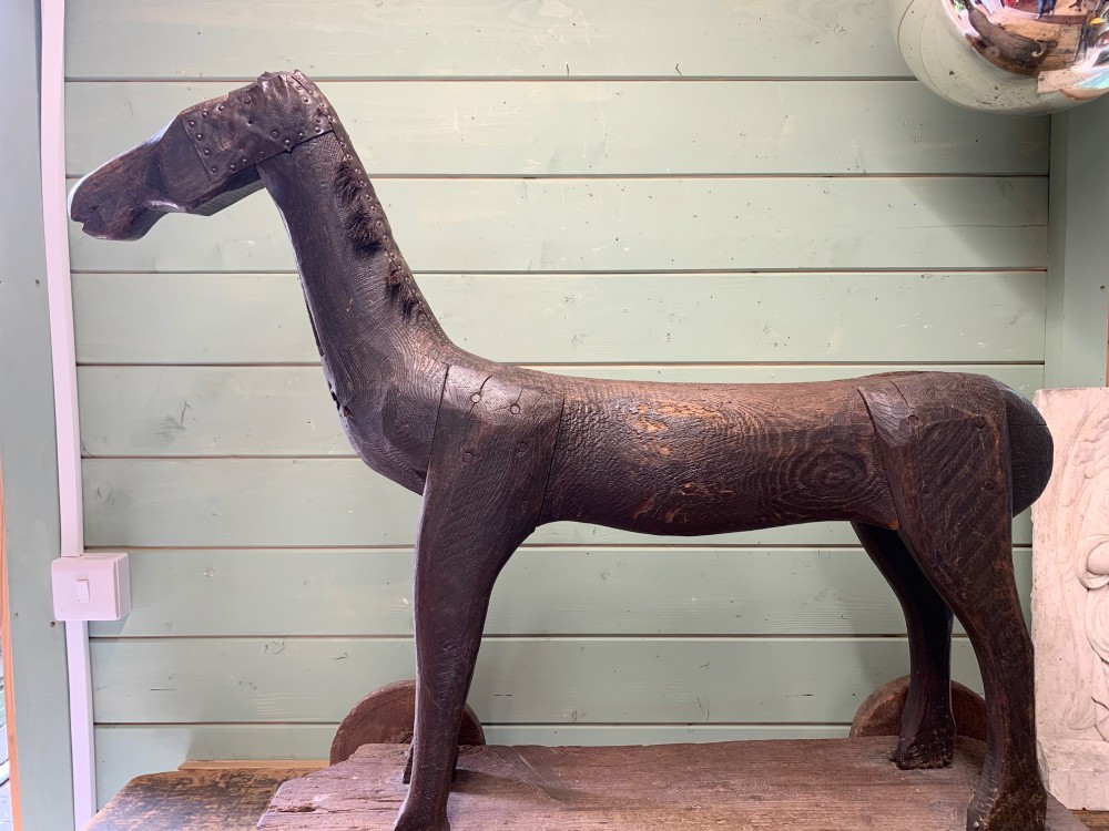 A naive hand-carved dark wood figure of a horse mounted on a flat wooden base with four simple circular wheels. View VI