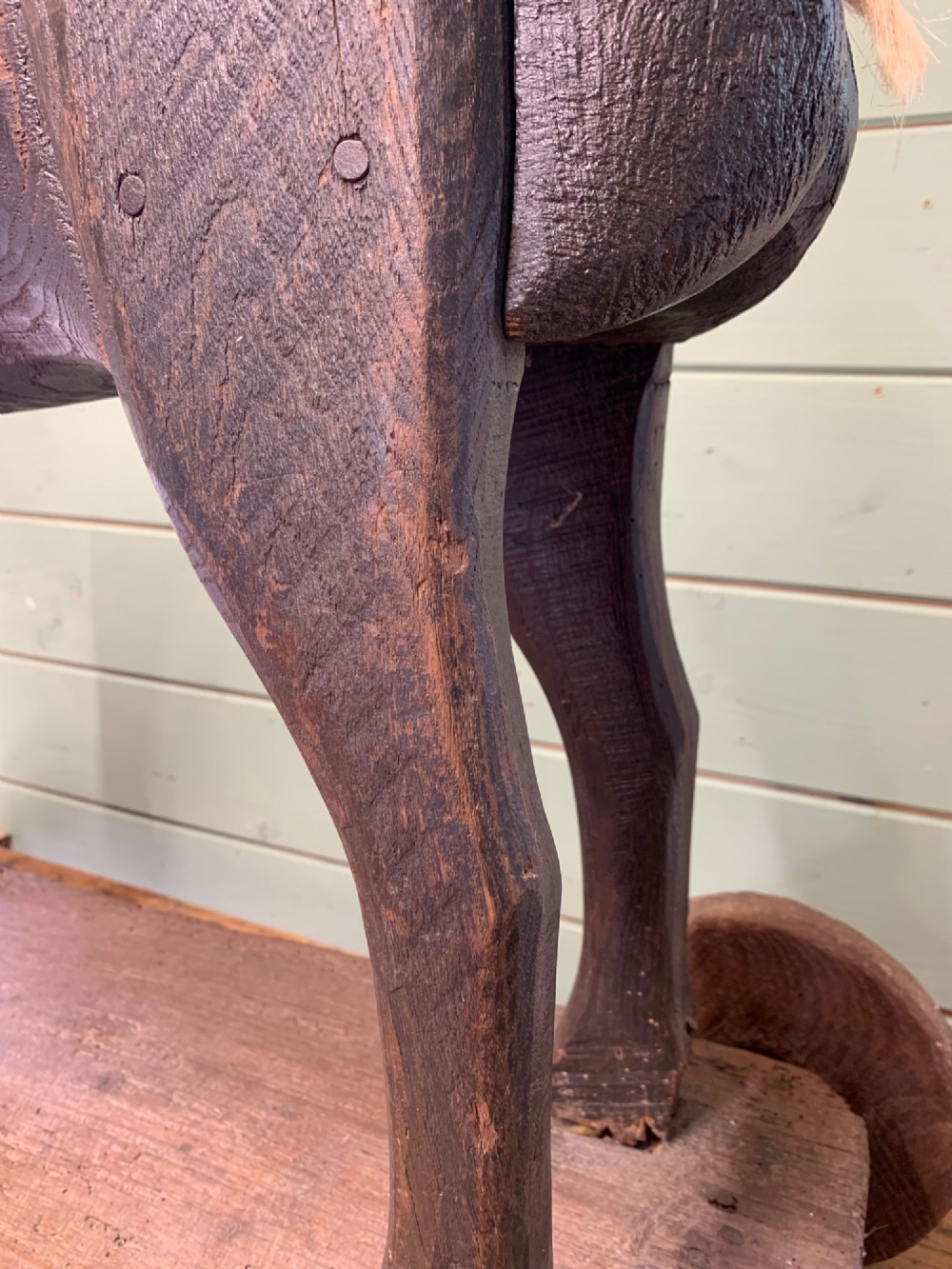 A naive hand-carved dark wood figure of a horse mounted on a flat wooden base with four simple circular wheels. View X
