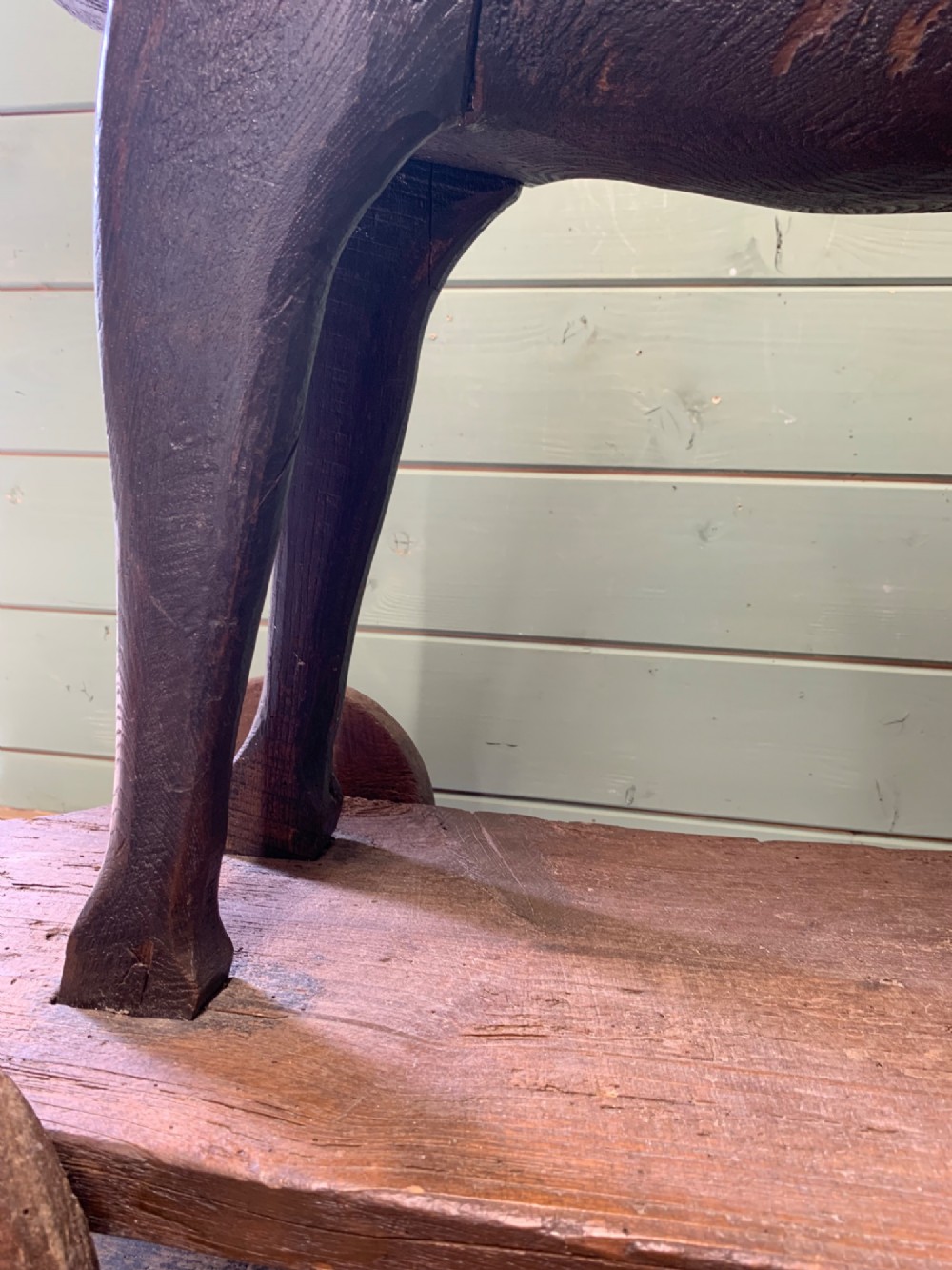 A naive hand-carved dark wood figure of a horse mounted on a flat wooden base with four simple circular wheels. View XII