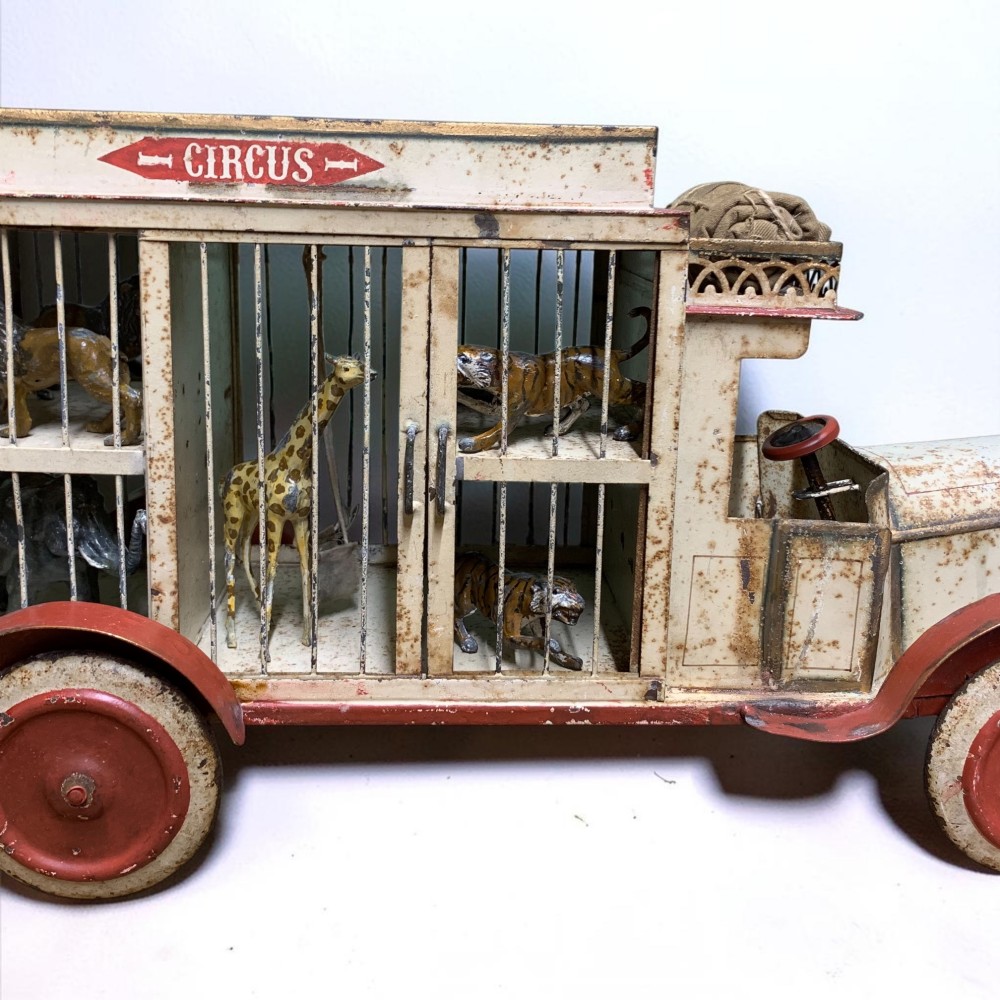 A 1920s painted tinplate Kibri circus lorry featuring cream side cage bars, red wheels, red accents, and miniature animal figures enclosed inside. View III