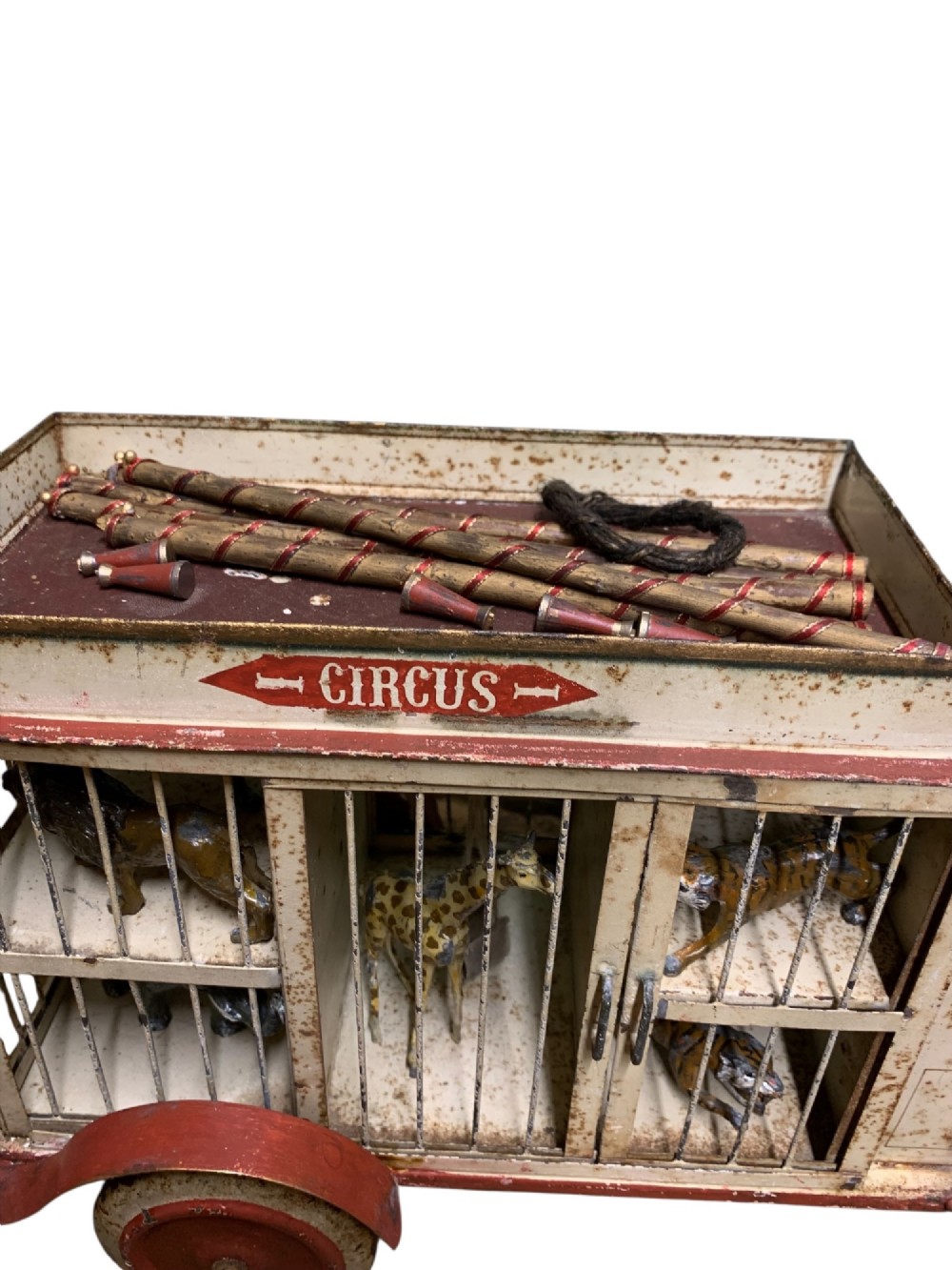 A 1920s painted tinplate Kibri circus lorry featuring cream side cage bars, red wheels, red accents, and miniature animal figures enclosed inside. View X