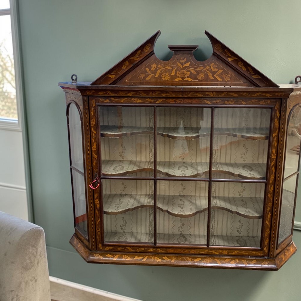 An 18th-century Dutch wall cabinet made of warm brown wood with botanical marquetry inlays, featuring a central glazed door, canted side panels, and a shaped pediment. View II