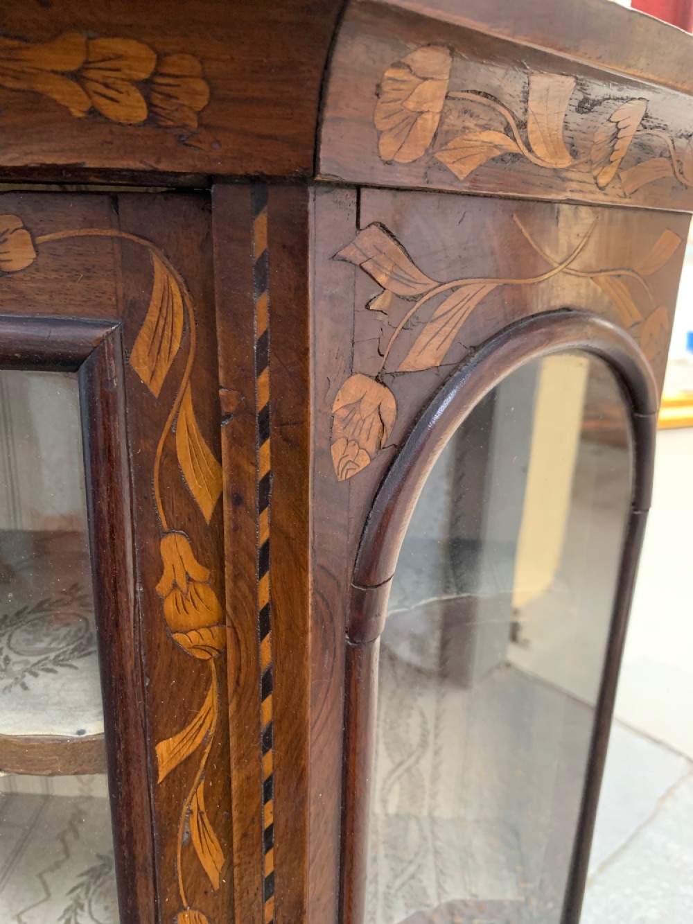 An 18th-century Dutch wall cabinet made of warm brown wood with botanical marquetry inlays, featuring a central glazed door, canted side panels, and a shaped pediment. View V