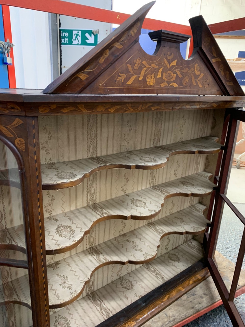 An 18th-century Dutch wall cabinet made of warm brown wood with botanical marquetry inlays, featuring a central glazed door, canted side panels, and a shaped pediment. View VII