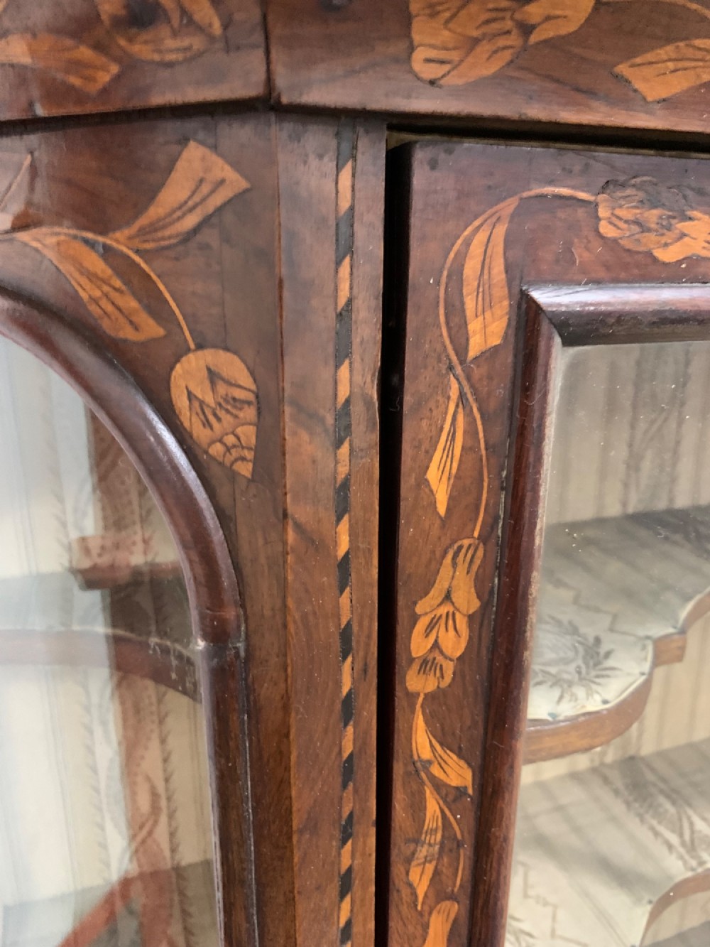 An 18th-century Dutch wall cabinet made of warm brown wood with botanical marquetry inlays, featuring a central glazed door, canted side panels, and a shaped pediment. View IX