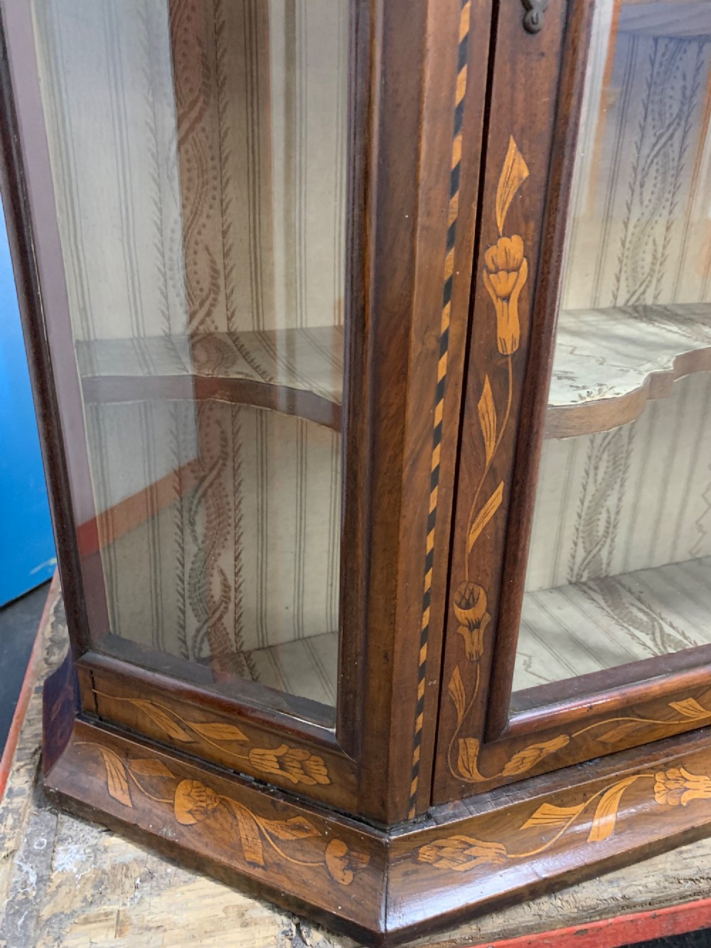 An 18th-century Dutch wall cabinet made of warm brown wood with botanical marquetry inlays, featuring a central glazed door, canted side panels, and a shaped pediment. View X