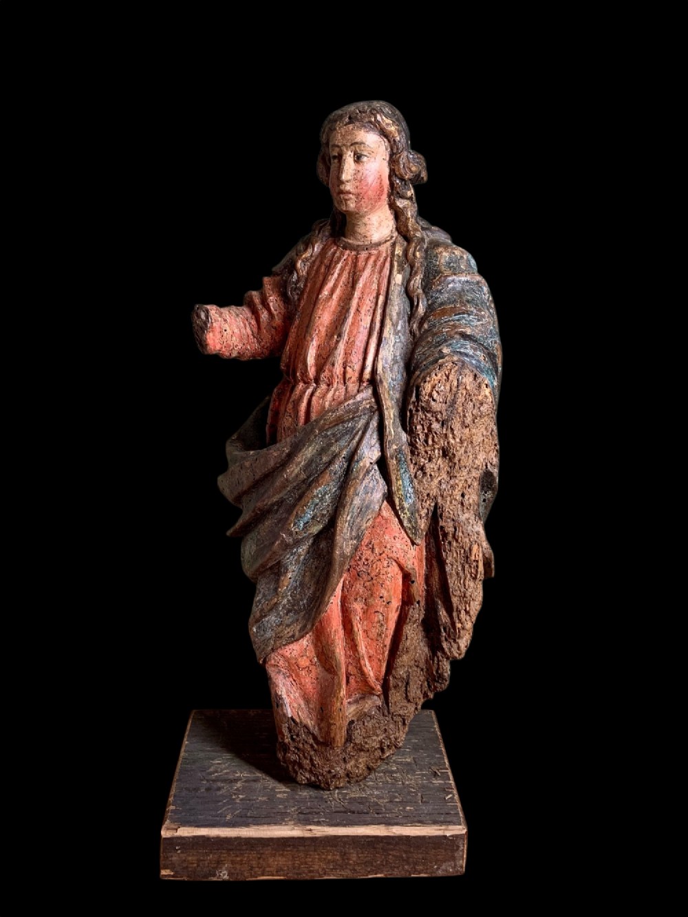An eighteenth-century carved wood figure of a saint featuring red and blue polychrome paint, set upon a rectangular wooden base.