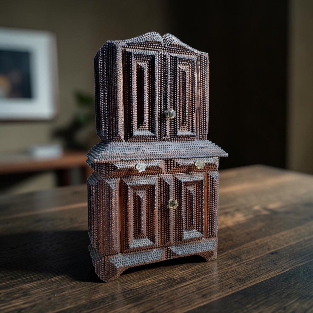 A miniature dark wood tramp art cabinet featuring layered notch-carved geometric borders, double upper doors, and small glass knobs.
