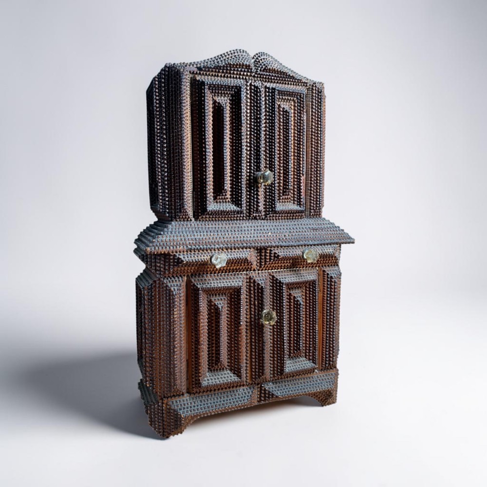 A miniature dark wood tramp art cabinet featuring layered notch-carved geometric borders, double upper doors, and small glass knobs. View II