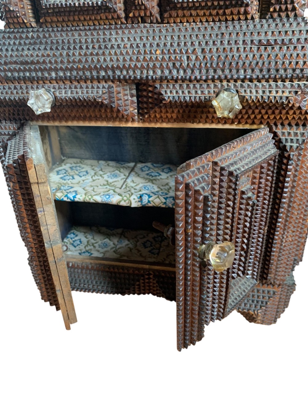 A miniature dark wood tramp art cabinet featuring layered notch-carved geometric borders, double upper doors, and small glass knobs. View IV
