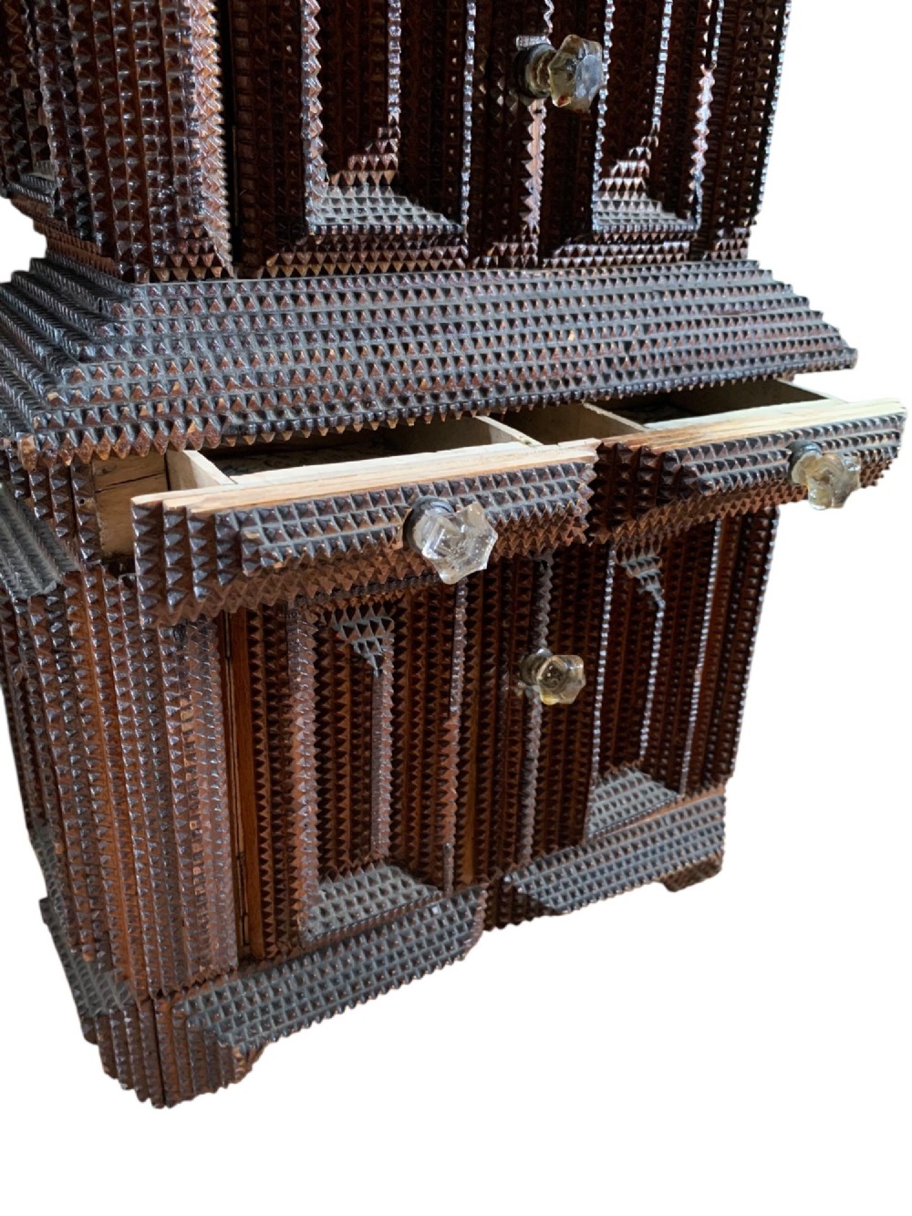 A miniature dark wood tramp art cabinet featuring layered notch-carved geometric borders, double upper doors, and small glass knobs. View V